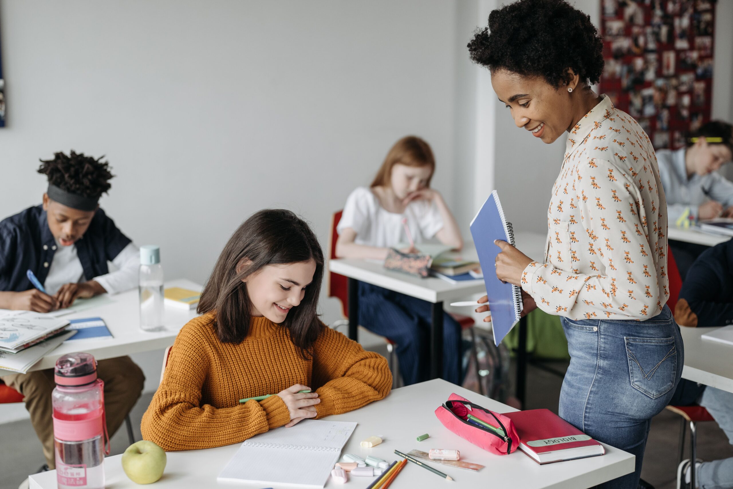 pexels-pavel-danilyuk-8423077 A teacher checking on a student who is sitting at her desk working on school project.